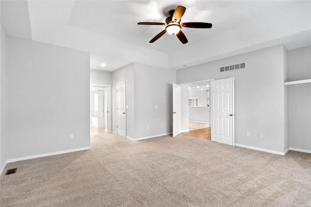 unfurnished bedroom featuring a tray ceiling, ensuite bath, ceiling fan, and light colored carpet