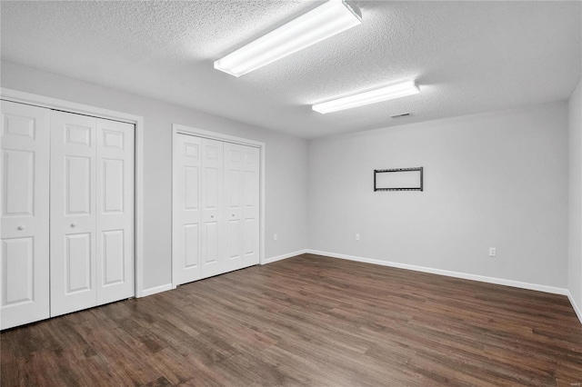 unfurnished bedroom featuring a textured ceiling, two closets, and dark wood-type flooring