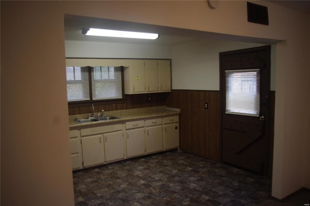 kitchen featuring white cabinets, sink, and wood walls