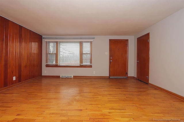 spare room featuring wood walls and light wood-type flooring