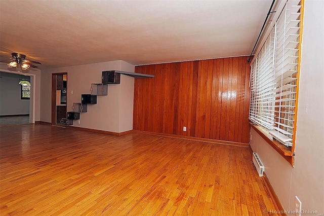 unfurnished living room featuring a baseboard heating unit, ceiling fan, a healthy amount of sunlight, and wood walls