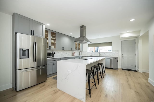 kitchen with island exhaust hood, light stone counters, a breakfast bar, stainless steel appliances, and a center island