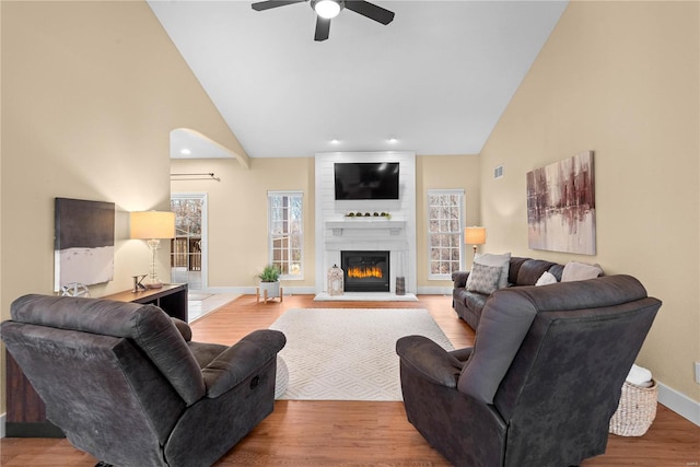 living room with ceiling fan, a fireplace, high vaulted ceiling, and light hardwood / wood-style floors