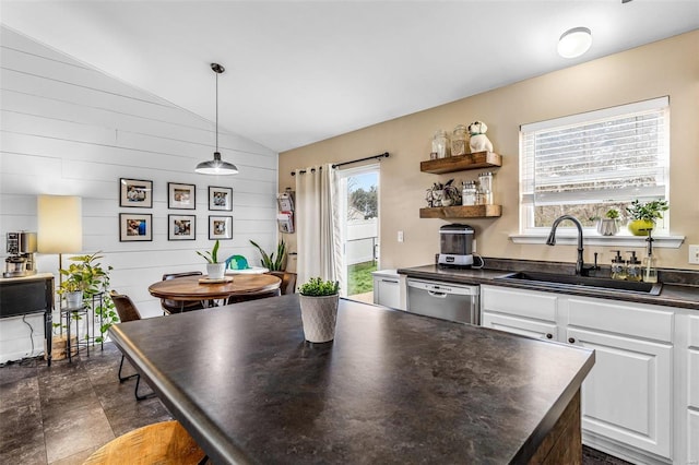 kitchen featuring lofted ceiling, white cabinets, sink, hanging light fixtures, and stainless steel dishwasher