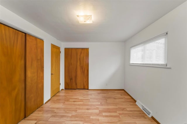 unfurnished bedroom featuring light wood-type flooring and multiple closets