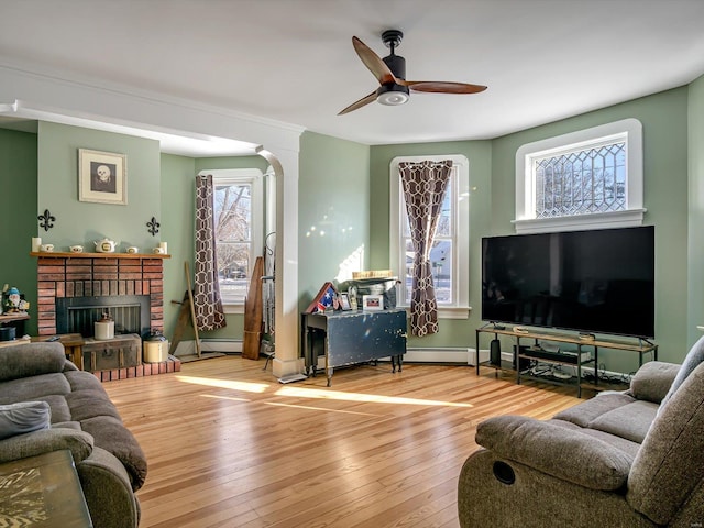 living room with ceiling fan, baseboards, light wood-style floors, baseboard heating, and a brick fireplace