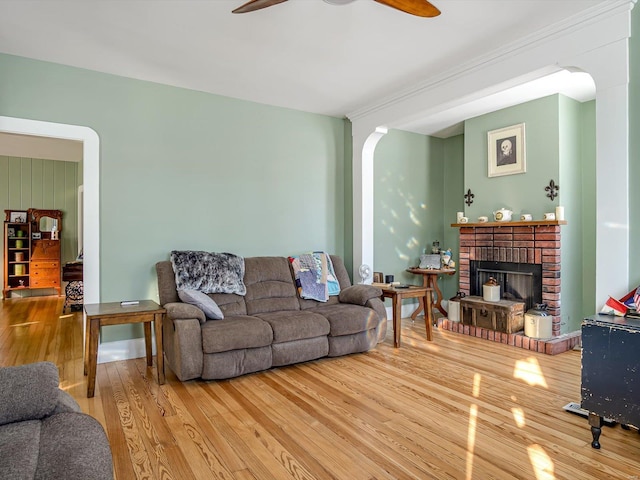 living area with ceiling fan, a fireplace, arched walkways, and wood finished floors