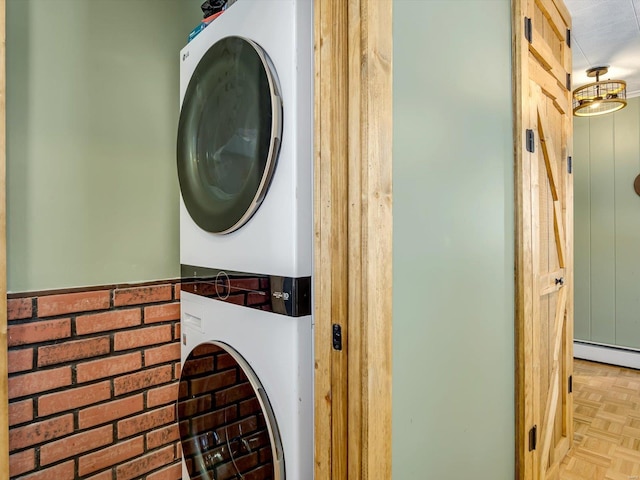 clothes washing area featuring stacked washer / drying machine, laundry area, and a baseboard radiator