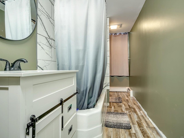 full bath with a baseboard radiator, wood finished floors, and shower / bath combo with shower curtain