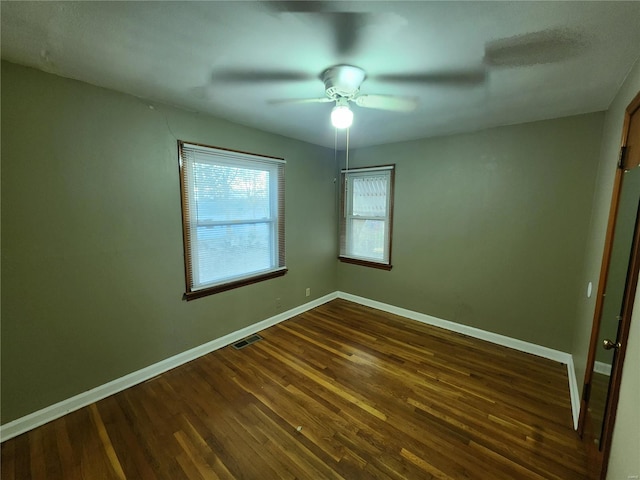 spare room with dark wood-type flooring, visible vents, and baseboards