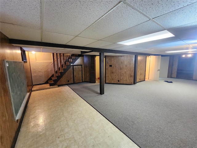 finished basement featuring light floors, wooden walls, stairs, and a drop ceiling