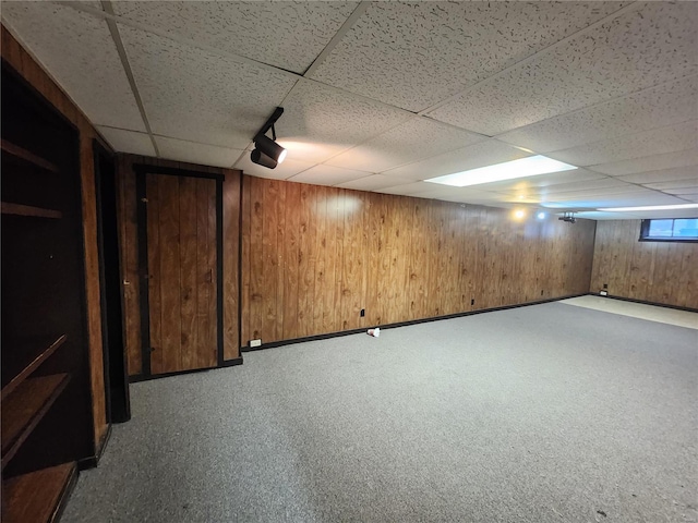 basement with carpet flooring, a drop ceiling, and wooden walls