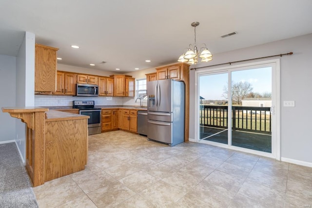 kitchen with kitchen peninsula, appliances with stainless steel finishes, backsplash, pendant lighting, and a chandelier