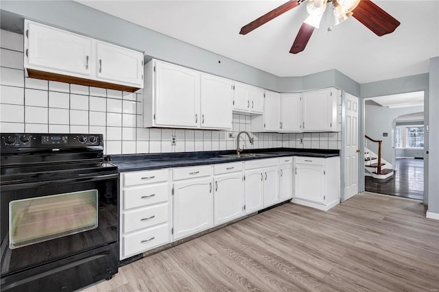 kitchen featuring light wood-type flooring, tasteful backsplash, sink, black electric range, and white cabinetry