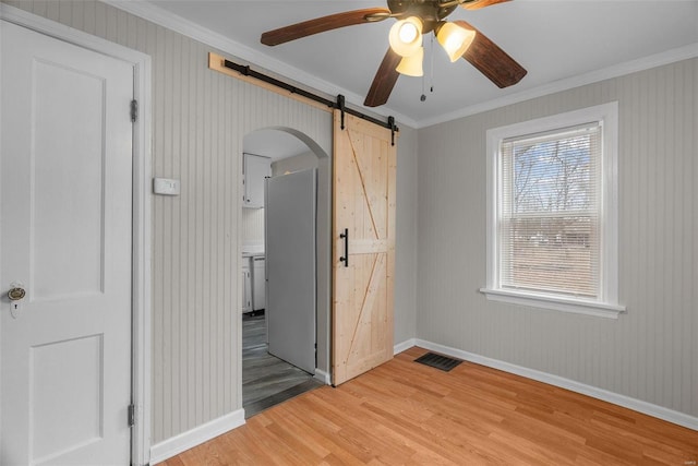 unfurnished bedroom featuring a barn door, crown molding, ceiling fan, and light hardwood / wood-style floors