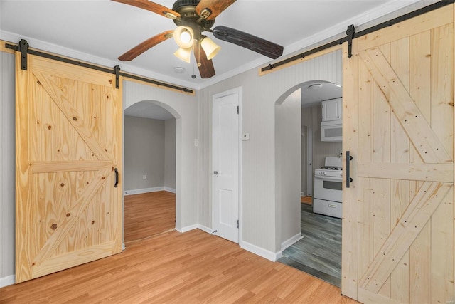 spare room featuring a barn door, ceiling fan, wood-type flooring, and ornamental molding