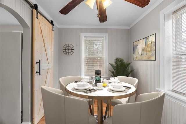 dining room featuring ceiling fan, a barn door, and crown molding