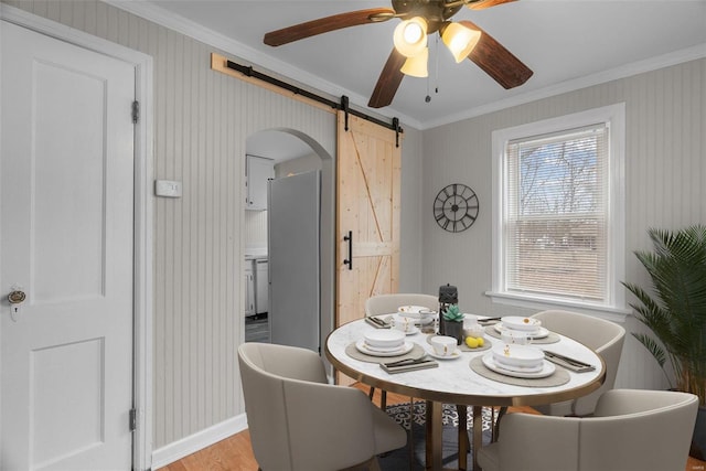 dining area with a barn door, crown molding, light hardwood / wood-style flooring, and ceiling fan