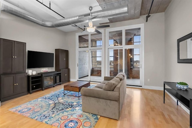 living room with visible vents, baseboards, ceiling fan, a high ceiling, and light wood-type flooring