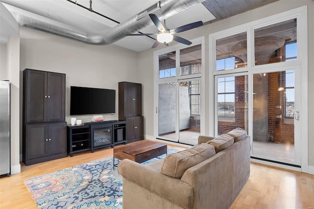 living room featuring ceiling fan, a towering ceiling, light wood-style flooring, and baseboards