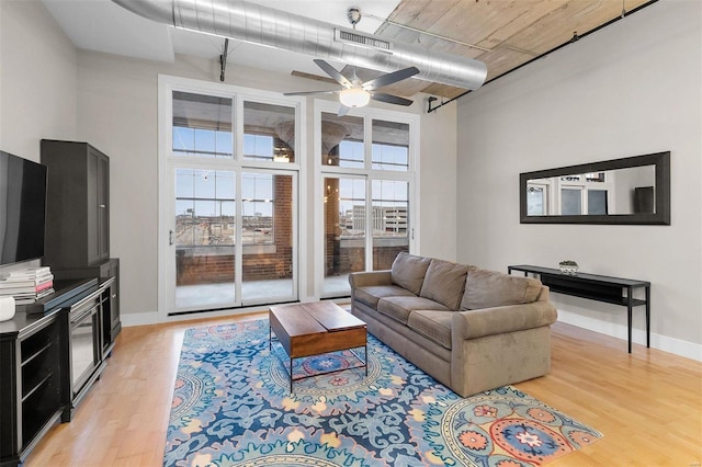 living area featuring visible vents, a towering ceiling, light wood-style floors, a ceiling fan, and baseboards