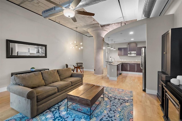 living room with ceiling fan with notable chandelier, light wood finished floors, and baseboards