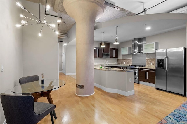 kitchen featuring light wood-style flooring, dark brown cabinets, appliances with stainless steel finishes, decorative backsplash, and wall chimney exhaust hood