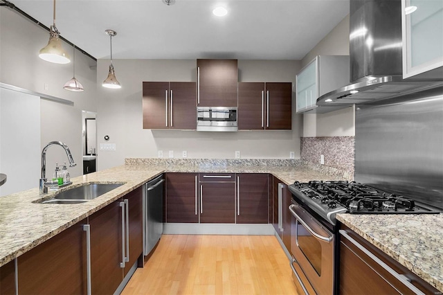 kitchen with light stone counters, light wood finished floors, stainless steel appliances, a sink, and wall chimney range hood