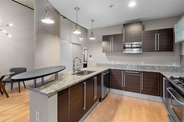 kitchen featuring a peninsula, light wood-type flooring, appliances with stainless steel finishes, and a sink