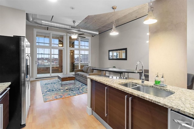 kitchen featuring dark brown cabinetry, decorative light fixtures, freestanding refrigerator, light wood-type flooring, and a sink