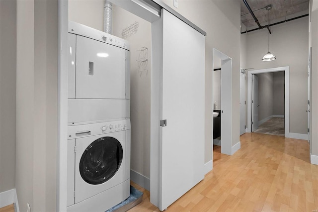 laundry area with laundry area, a towering ceiling, baseboards, light wood finished floors, and stacked washer and clothes dryer