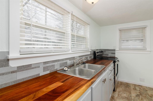 kitchen with stainless steel electric stove, decorative backsplash, white cabinetry, and sink