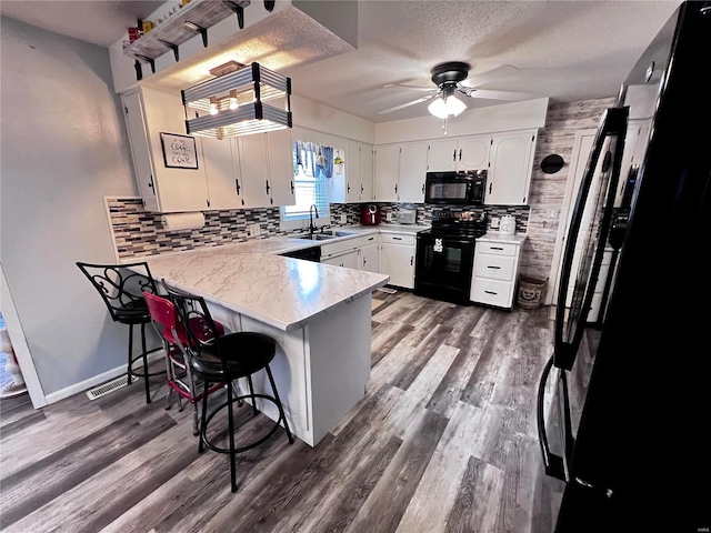 kitchen with kitchen peninsula, a breakfast bar, sink, black appliances, and white cabinetry