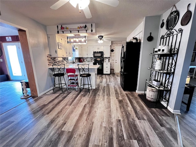 kitchen featuring kitchen peninsula, a kitchen breakfast bar, decorative backsplash, black appliances, and white cabinets