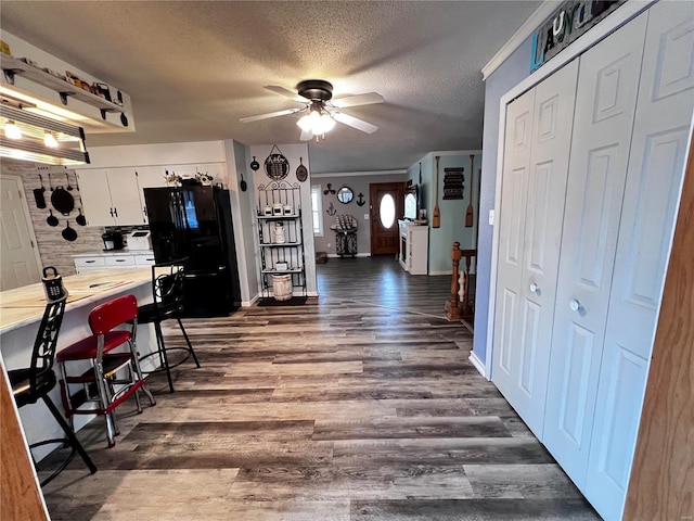 kitchen featuring white cabinets, black refrigerator, ceiling fan, dark hardwood / wood-style flooring, and a breakfast bar area