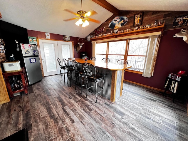 kitchen featuring stainless steel refrigerator, ceiling fan, dark wood-type flooring, vaulted ceiling with beams, and a kitchen bar