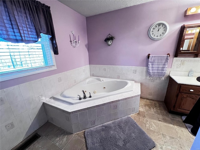 bathroom featuring tile patterned floors, tiled bath, vanity, and a textured ceiling