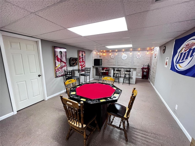 game room with a drop ceiling, bar, and brick wall