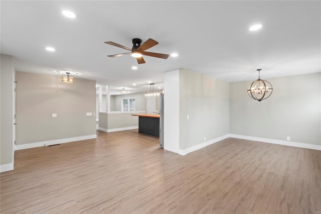 unfurnished living room with ceiling fan with notable chandelier and light hardwood / wood-style floors