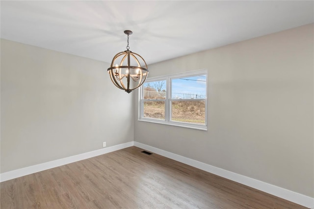 empty room featuring wood-type flooring and a notable chandelier