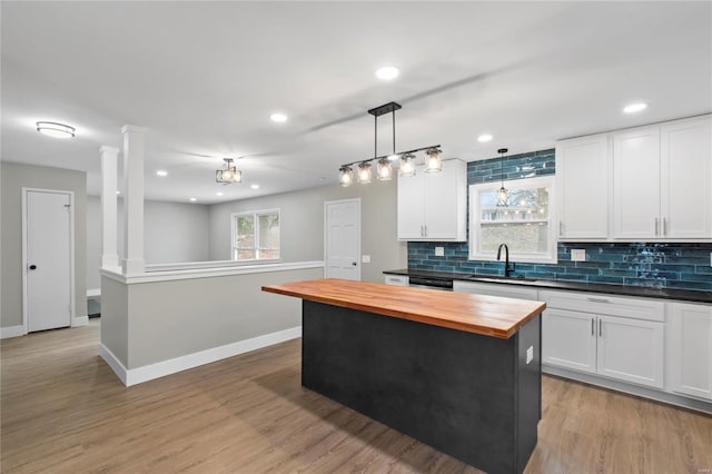 kitchen featuring a center island, white cabinets, sink, decorative light fixtures, and butcher block counters