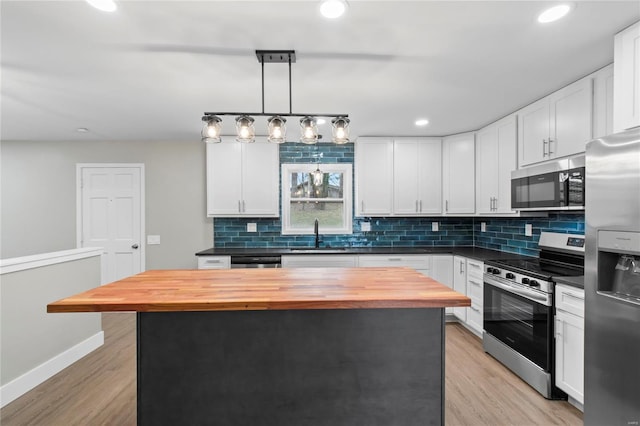 kitchen featuring wooden counters, stainless steel appliances, decorative light fixtures, white cabinetry, and a kitchen island