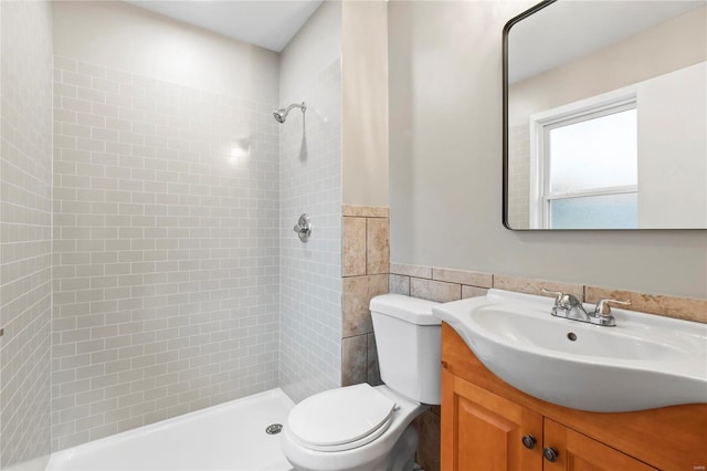 bathroom with a tile shower, vanity, tile walls, and toilet