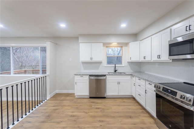 kitchen featuring light stone countertops, light wood-type flooring, stainless steel appliances, sink, and white cabinetry