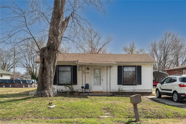 view of front of house featuring roof with shingles, a detached carport, and a front yard