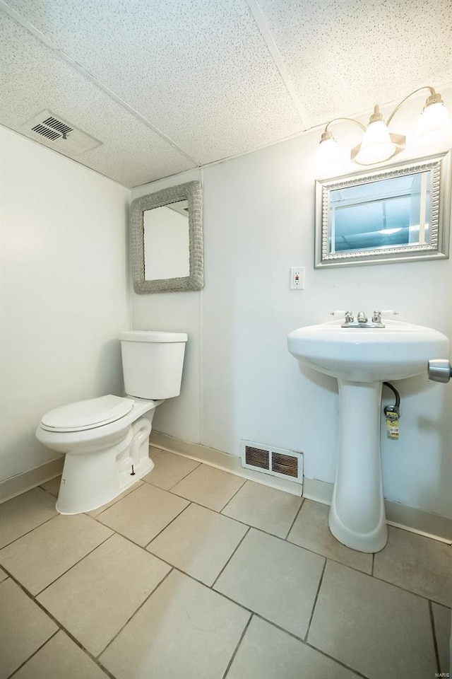 bathroom with a paneled ceiling, tile patterned flooring, and toilet