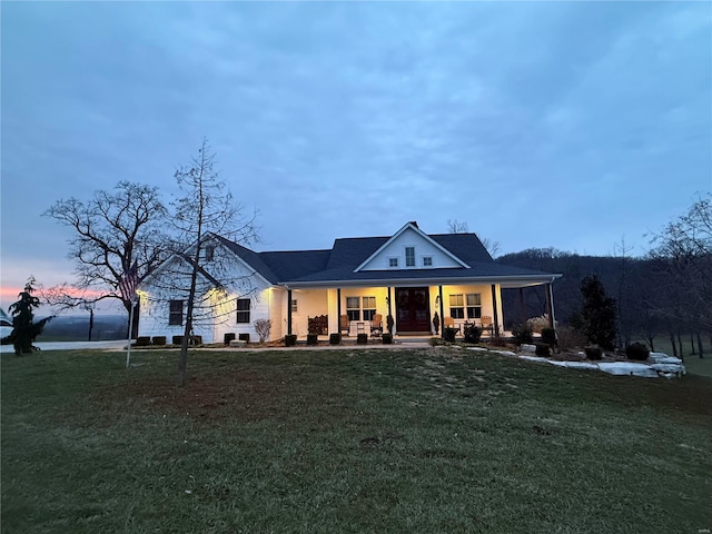 back house at dusk with a porch and a yard