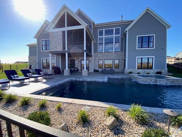 back of house featuring a sunroom, a swimming pool with hot tub, and a patio