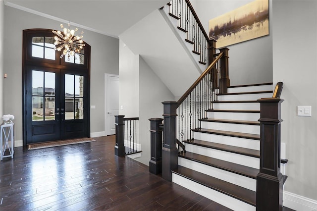 foyer entrance with french doors, a towering ceiling, dark wood-type flooring, and an inviting chandelier