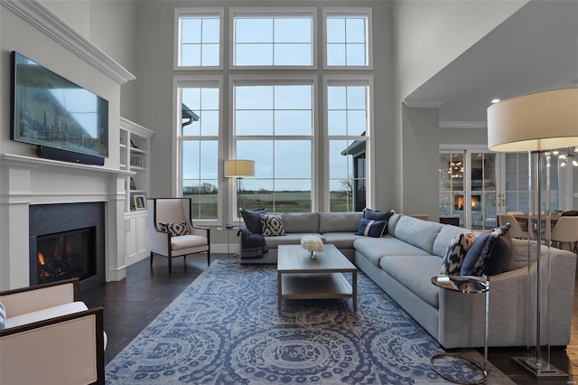 living room with built in shelves, crown molding, dark wood-type flooring, and a high ceiling